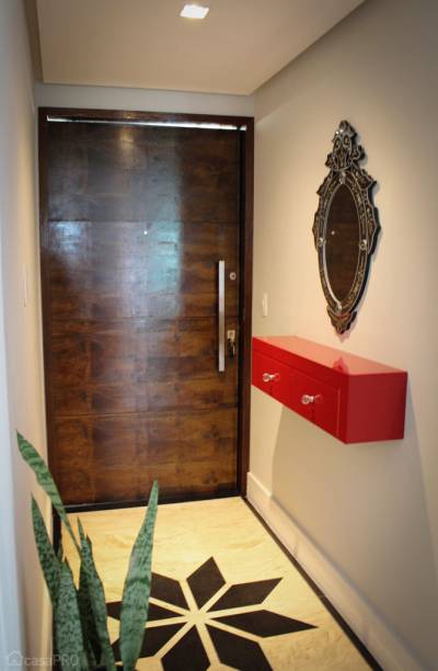 Projeto de hall de entrada com piso em mármore crema marfil e preto absoluto, móvel de vidro laqueado marsala. Parede com pintura na cor cinza de Grife (Coral) e porta de entrada pivotante em madeira. Projeto do Studio Due Arquitetura.