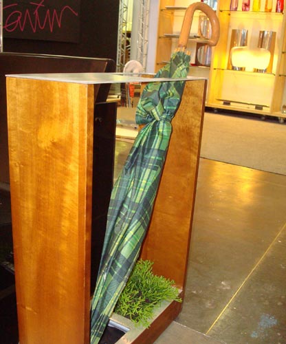 O porta guarda-chuva de madeira tem um vasinho na base. A idéia é reusar a água que escorre do guarda-chuva para regar as plantinhas. Projeto da Tevi Design.