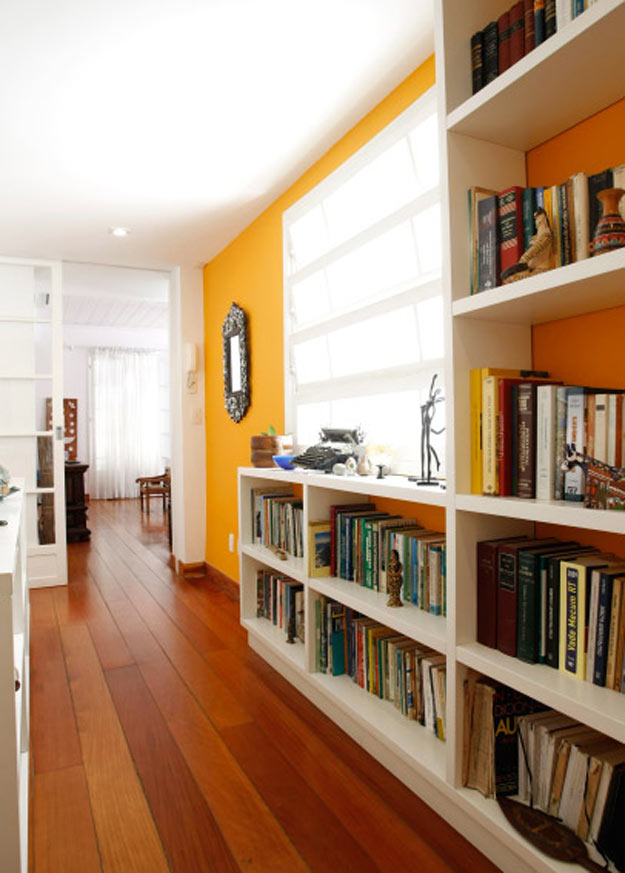 Corredor; decorar corredor; estante branca; estante com livros; parede amarela; espelho
