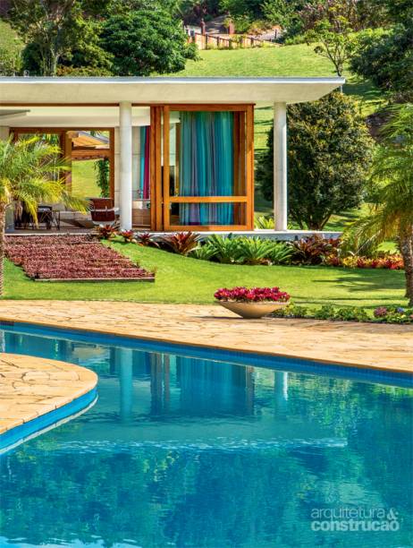 A piscina já existia e foi preservada. Na leve subida em direção à casa, o projeto de paisagismo (Painel Verde) incluiu a escada de dormentes intercalados entre mudas de tapete-inglês. Projeto de Skylab Arquitetos.