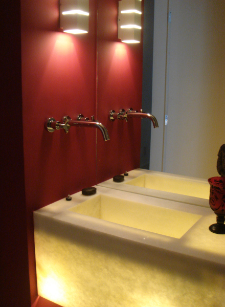 A pia iluminada e a parede vermelha são o destaque deste lavabo projetado por André Martins. Repare que, para não ter que furar o espelho e para economizar espaço, as torneiras foram parara na parede lateral.