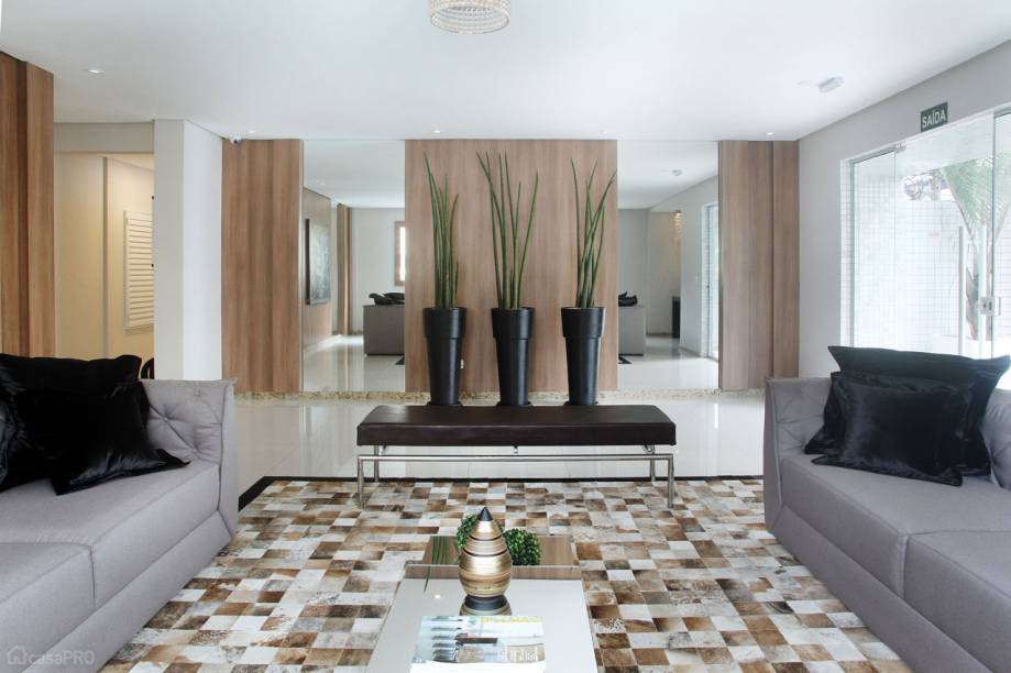 Projeto de hall de entrada de condomínio residencial com piso porcelanato, paredes com painéis de mdf e espelhos, tapete de couro natural, vasos com plantas naturais. Projeto de Rosa Pinheiro.