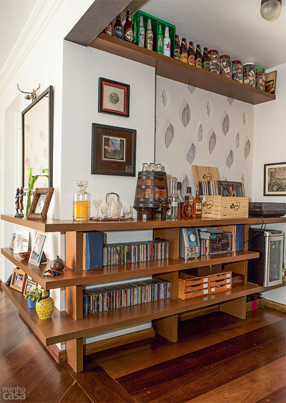 BAR E M&Uacute;SICA DE CONFUNDEM. Um canto para bebericar e curtir as faixas musicais favoritas era o que desejava o morador deste apartamento paulistano. Quando bateram o olho no encontro de duas paredes na sala, as arquitetas Ana Carolina e Mariana Lima Orsolini tiveram a ideia: prateleiras em L, de MDF com laminado freij&oacute;, abra&ccedil;ariam a quina, dando conta do recado sem atrapalhar a circula&ccedil;&atilde;o. As tr&ecirc;s pranchas no lado mais curto t&ecirc;m fun&ccedil;&atilde;o de aparador, enquanto as extensas, com 2,38 m, acomodam os CDs, o equipamento de som, uma caixa de madeira repleta de vinis, um toca-discos e o bar. O conjunto (Marcenaria Vida Nova, R$ 4820, inclui a prateleira superior) vai preso &agrave; alvenaria por suportes invis&iacute;veis.