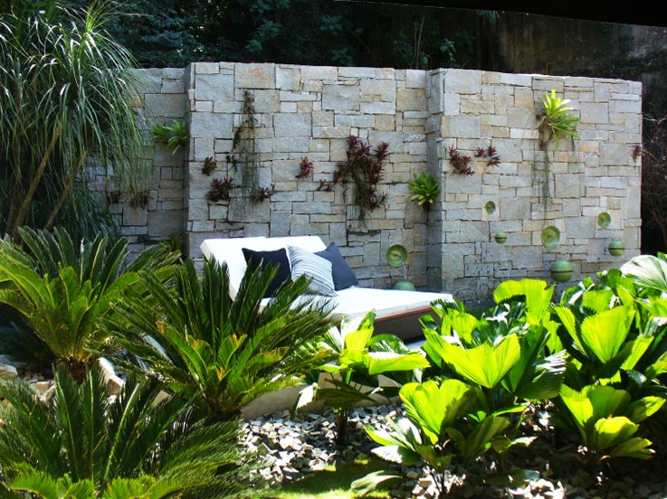 Pedras em cortes irregulares compõem o muro deste projeto assinado pelo paisagista Luiz Lima para a Casa Cor Rio de Janeiro: para aproveitar os espaços entre as pedras, ele “plantou” bromélias e ripsális. Os detalhes verdes na parte inferior são, na verdade, fontes que imitam “bolas flutuantes”, elaboradas com a ajuda de um ceramista e que têm como objetivo dar leveza ao espaço.
