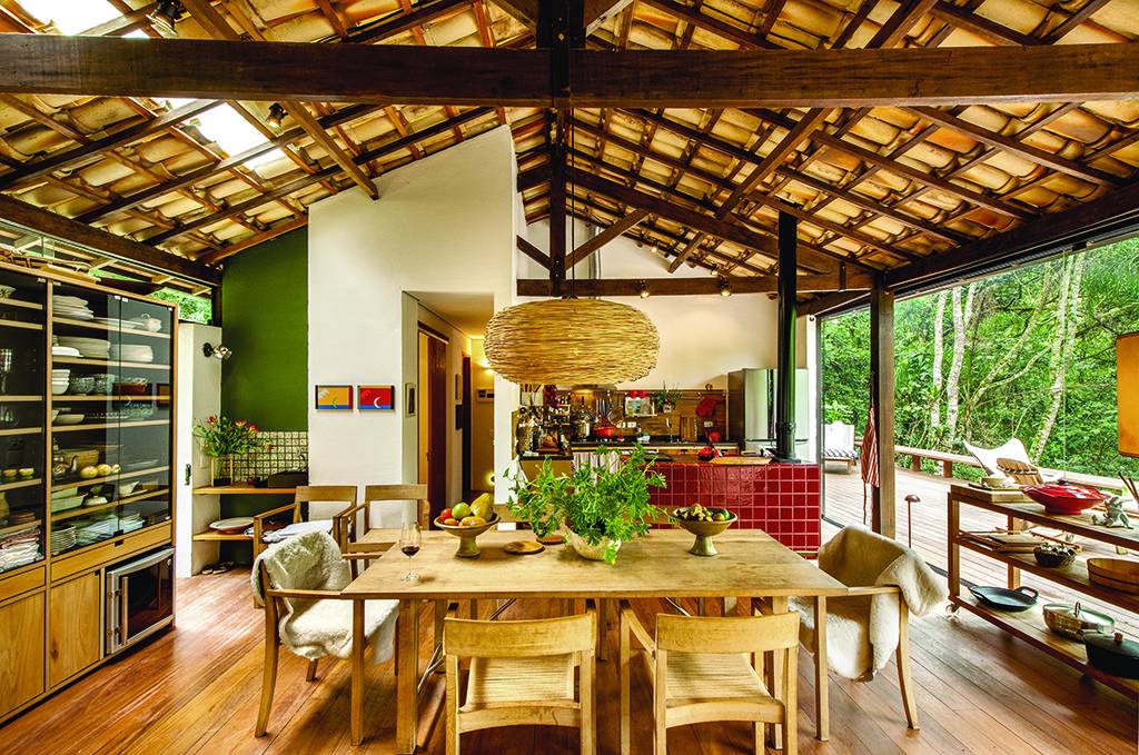 De madeira teca, a mesa e as poltronas dinamarquesas (Casual) re&uacute;nem os amigos e tamb&eacute;m d&atilde;o apoio ao casal quando traz trabalho de S&atilde;o Paulo. Ao fundo, o fog&atilde;o a lenha (Oficina Victorello) foi revestido de azulejos especiais da Antigua, lembrando o vermelh&atilde;o dos fog&otilde;es mineiros. Projeto de Vania Chene.