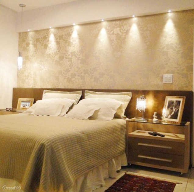 O papel de parede estampado ganha destaque com a iluminação indireta neste quarto assinado por Celina Alcantara de Alencar. Repare que os abajures são diferentes em cada lado da cama.