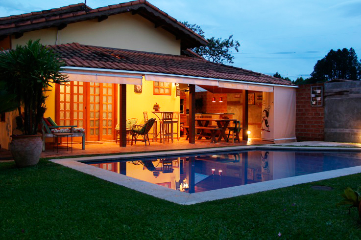 CASA EM IBIÚNA. Localizada em Ibiúna, interior de São Paulo, esta casa de campo foi reformada pela arquiteta Luciane Cucomo Galera. Com 480 m² de terreno e 175 m² de área construída, a casa traz portas e caixilhos de madeira, que proporcionam o ar rústico desejado pelos proprietários. A foto mostra a varanda da casa, que foi pensada na reforma como um ambiente para integrar a família, com churrasqueira e televisão.