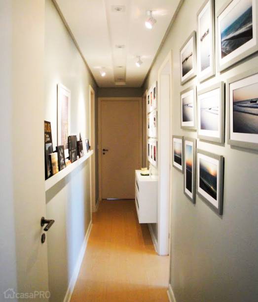 O objetivo deste projeto foi transformar o corredor em uma espécie de galeria de arte, pois a proprietária tem como hobby a fotografia. Foi executado um forro de gesso com spots embutidos para iluminação geral e pequenos refletores se direcionam para os quadros. A parede recebeu pintura em tinta acrílica acetinada em tom de cinza. De um lado, as fotos foram distribuídas em diferentes arranjos separadas por temas - cada grupo recebeu uma moldura padronizada. Na parede oposta, uma canaleta para apoiar as fotos permite que elas sejam trocadas com facilidade. Um pequeno balcão em laca branca serve para armazenar as máquinas fotográficas e outros pequenos objetos. Projeto de Marta Costa Oliveira.