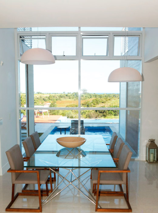 A parede de vidro nesta sala de jantar proporciona a bela vista do deque e da piscina. Projeto de Augusto Alvarenga.