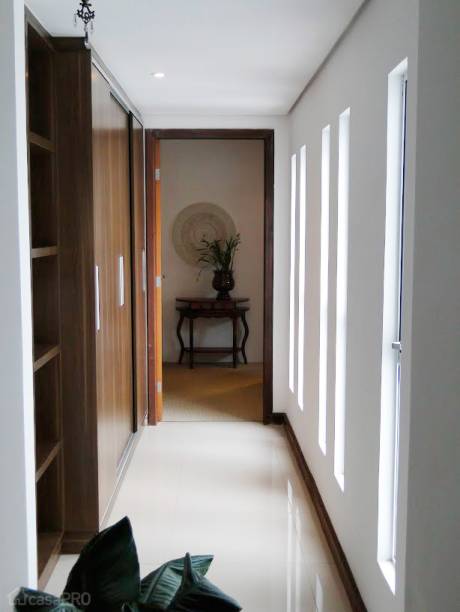 O corredor desta casa possui iluminação e ventilação natural e um nicho pensado para marcenaria para guardar sapatos e utensílios como kit de costura, ferramentas de emergência etc. O porcelanato (Eliana Crema Marfil 60 x 60 cm) da área social é arrematado com rodapé de madeira maciça imbuia, seguindo o padrão de acabamento das portas e contrasta com as paredes brancas. Projeto de Ana Paula Haag.