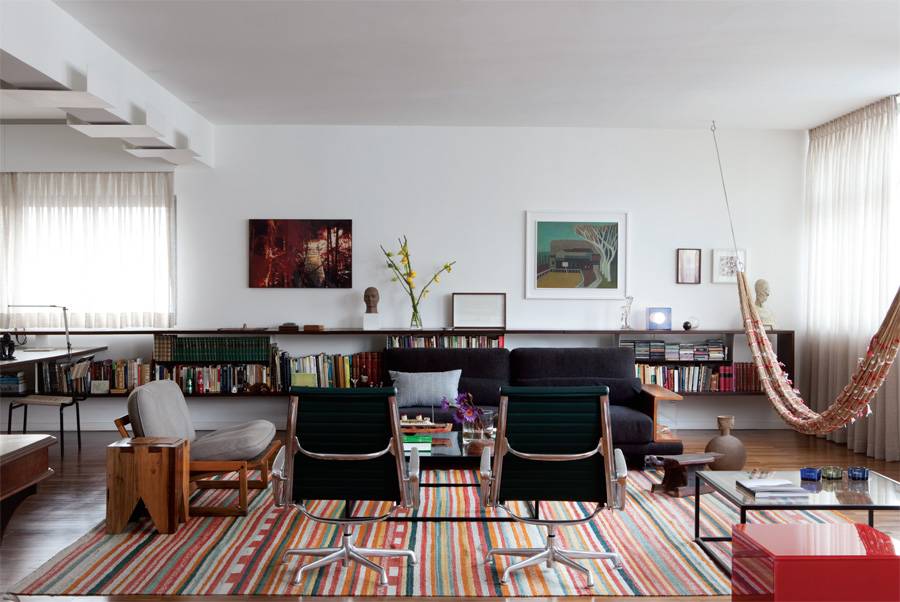 Rede artesanal no meio da sala. A rede dos &iacute;ndios do Xingu representa o fazer manual, t&atilde;o valorizado nesta casa quanto o design assinado: poltronas Charles Eames e cubo vermelho de Jacqueline Terpins. Sof&aacute; da Cod, vasos da Benedixt e tapete da By Kamy.