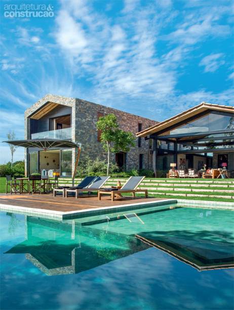 Dedicada ao lazer, a casa conta com uma piscina à frente, encaixada no desnível natural. assim, resta uma área ampla e segura para as crianças brincarem. Com raia e prainha, o tanque ganhou forração de pedras greenstone. Projeto de Gui Mattos.