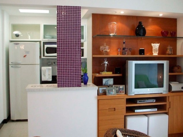 Neste espaço, de 40 m², a sala de estar, a sala de TV e a cozinha foram integradas pela designer de interiores Ana Lucia Nunes Gomes. Ao demolir a parede que separava a sala da cozinha, apareceu uma coluna, que acabou servindo de destaque para a integração dos ambientes.