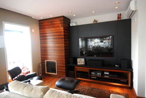Painel de ripas de madeira de vários tipos (cumaru, ipê, imbuia) cobrem a caixa da lareira neste home theater, em São Paulo. Projeto da arquiteta Cecilia Mattos Mueller.