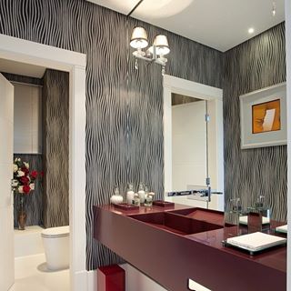 Este lavabo moderno faz parte de uma casa em São Paulo (SP), assinado pelo escritório Jannini Sagarra arquitetura. O papel de parede na cor preta e branco e a bancada com cuba esculpida em corian vermelho garantem sofisticação ao espaço.