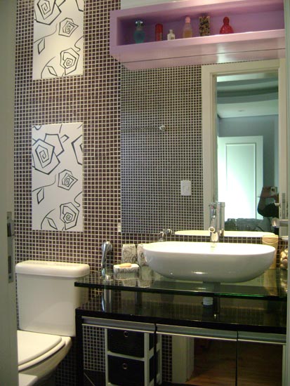 O clima moderno deste ambiente de Lívia Gobetti é proporcionado pelas pastilhas de resina na cor roxa. O charme fica por conta dos azulejos brancos com flores estilizadas. A cuba é apoiada por móvel em laca preta com tampo de vidro incolor 15mm. O nicho de laca lilás abriga perfumes acima do espelho.