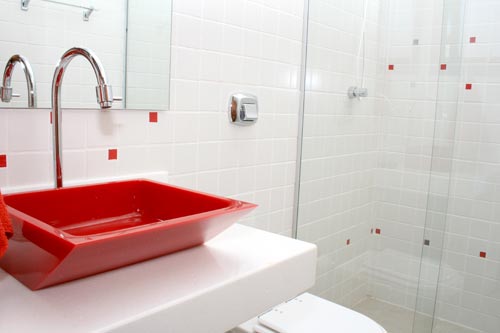 O charme deste banheiro feminino, de 4,20 m2, ficou por conta da cuba de apoio vermelha e das pastilhas salpicadas na área da bancada e do box. Detalhe simples e barato, de acordo com a arquiteta. Para que as pastilhas fossem inseridas, os azulejos de 9,5 x 9,5 cm foram cortados na obra no canto superior ou inferior.