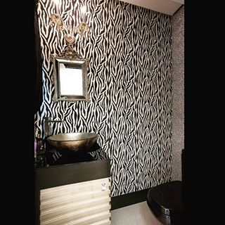 Inspirado em um “safári chic”, este lavabo de 2 m² ganhou papel de parede com estampa animal print e efeito de veludo em devorê nas cores dourada e preta. “Espelho e arandela com detalhes clássicos e cristais compõem o espaço”, explica a arquiteta Melissa Baron, que assina o projeto.
