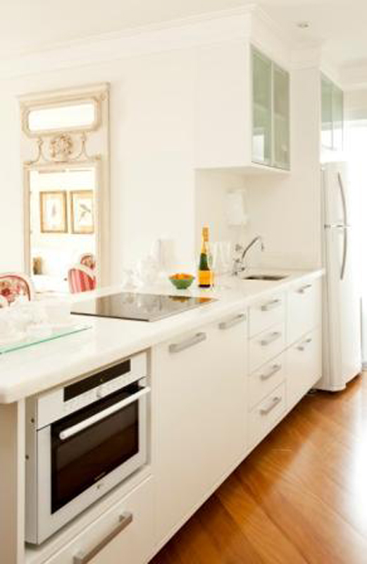 Os móveis todos em branco dão uma sensação de amplitude a esta cozinha projetada por Carolina Danielian. A cor ajuda a fundir a mobília à parede e até ao gesso do teto.