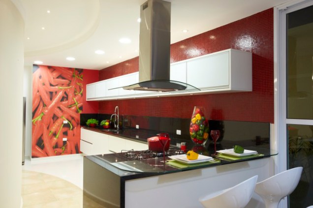 CASA NA SERRA DA CANTAREIRA. Na cozinha, de 39,08 m², da casa de campo projetada por Aquiles Nicolas Kilaris, o vermelho é destacado na imagem adesivada e nas pastilhas vermelhas (Colormix).  A bancada é de granito preto são gabriel e os armários feitos de fórmica branca e vidro serigrafado.