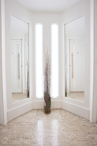 Hall social residencial. Paredes revestidas em MDF branco liso, com iluminação em led embutido, piso mármore travertino. Projeto Rose Ferraresi.