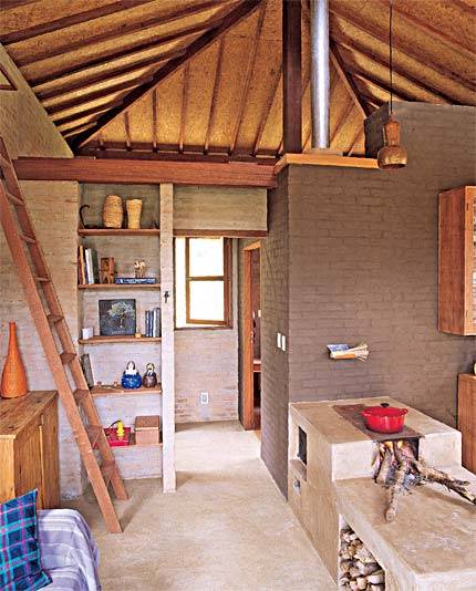 O p&eacute;-direito alto, de quase 5 m, amplia ainda mais o espa&ccedil;o que re&uacute;ne sala e cozinha e propicia uma vista privilegiada do entorno, cercado por cachoeiras, horta e pomar. O duto de a&ccedil;o galvanizado da chamin&eacute; do fog&atilde;o a lenha fica aparente na altura do mezanino para propagar o calor do fogo, artif&iacute;cio que garante temperatura amena nas madrugadas frias de inverno. Projeto Carlos Verna.
