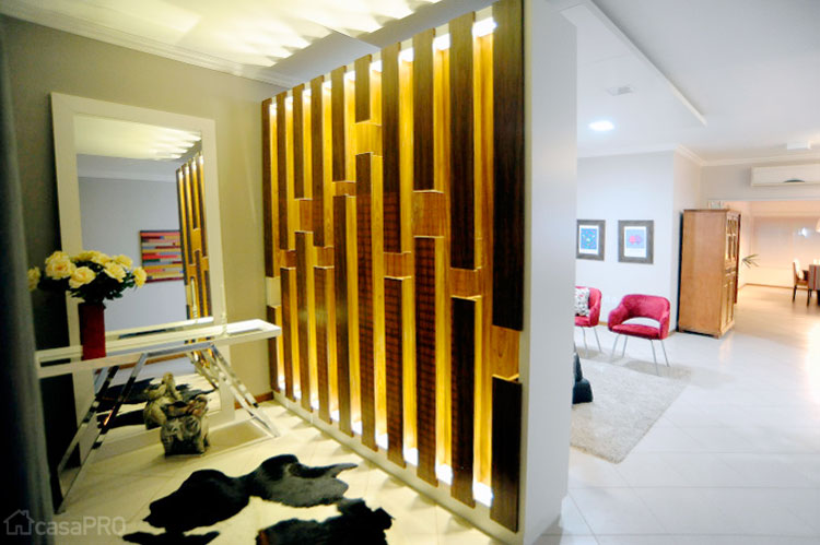 Hall criado para dar mais privacidade à casa. Painel divisório em mdf com iluminação de led para o lado do hall e estante de livros para a sala de relaxamento e leitura. Aparador de metal cromado e bandeja espelhada. Cortinas metal 50 mm e linho. Espelho escorado na parede. Projeto de Roberta Kirst.