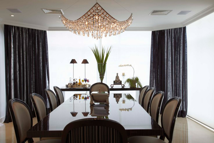 Um lustre detalhado e cortinas escuras dão um ar sofisticado a esta sala de jantar projetada por Lia Salales.