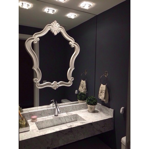 A parede escura não pesa no ambiente porque contrasta com a bancada de mármore e o gesso branco. A moldura sobre o espelho dá um efeito clássico. Projeto de Marlon Behenck.