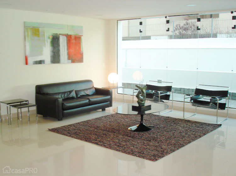 Hall de entrada em edifício residencial. Piso de porcelanato polido, painel de gesso saliente na parede para receber escultura de Fabian Rodrigues, guarita em alvenaria com tampo em mármore Crema Marfil e vidro fumê dividindo a área externa e interna. Projeto de Lucia Bellini.