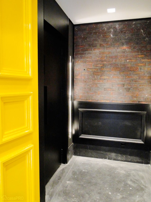 O Projeto deste Hall Social integrou as portas dos dois elevadores, revestindo-as com uma caixa de mdf laqueado de preto em acabamento fosco. A parede do fundo recebeu revestimentos de Tijolos tipo Shirraz da Palimanan Revestimentos. O Piso preto rústico, com cara de pedra é na verdade um porcenalato italiano de 120x120cm. A porta no estilo clássico ganhou uma apegada moderna ao ser laqueada de amarelo brilhante. Projeto da arquiteta Débora Nanni.