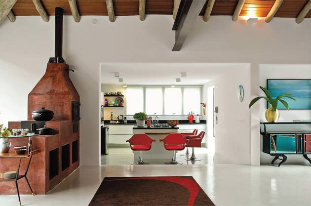 Neste projeto de Neza Cesar, o branco &eacute; quase total, na alvenaria e no piso de cimento polim&eacute;rico. Pinceladas mais fortes aparecem nas cadeiras vermelhas da bancada, no multicolorido dos objetos culin&aacute;rios, no tapete de desenho abstrato e at&eacute; no terracota do fog&atilde;o a lenha, que convive em harmonia com o ambiente contempor&acirc;neo.
