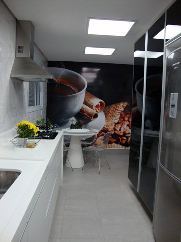 Esta cozinha projetada pelo escritório Madi Arquitetura e Design termina em uma área de refeições que recebeu uma plotagem na parede. As cores da foto ao fundo se repetem na parte da bancada.
