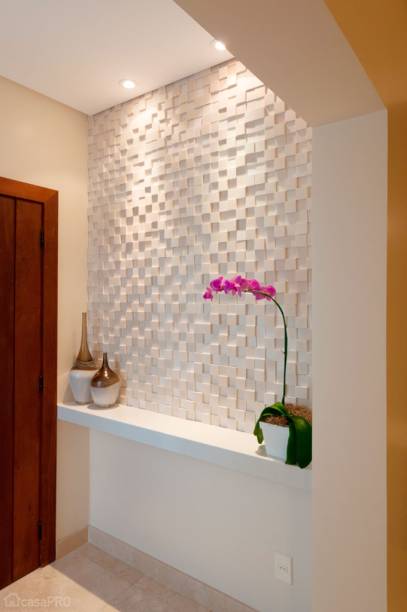 O hall de entrada desse apartamento recebeu piso de mármore Crema Marfil. Bancada de Star white e painel de cimentícios quadriculado. As paredes foram pintadas com Suvinil Toque de Seda na cor algodão egípcio. Iluminação embutida dicroica focada no painel. Projeto de Maristela Lima Bernal.