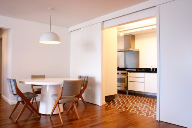 Uma porta de correr separa a cozinha desta sala de jantar. Pisos diferentes também marcam os ambientes. Projeto de Gisele Emery.