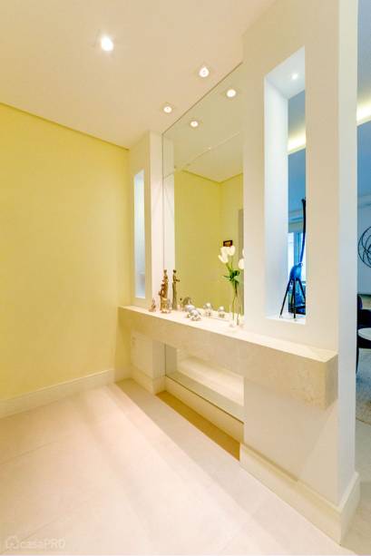 O hall de entrada de apartamento recebeu piso deporcelanato Crema Valência (Portinari). Rodapé: madeira na cor branca (modelo 480 Santa Luzia). Parede: espelhos com acabamentos micro-bisotê e pinturas nas cores Branco Neve (Suvinil) e Luzes da Cidade (Suvinil). Bancada em mármore Crema Marfil. Nichos vazados com iluminação em led (integração com a sala). Projeto da arquiteta Eveline Maciel.