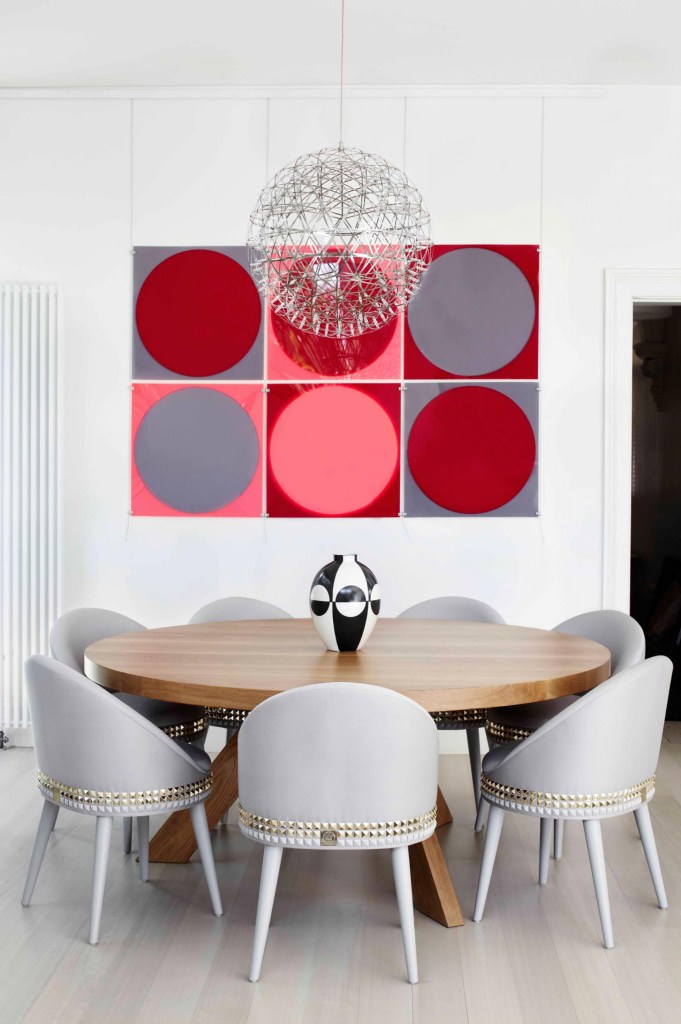 Sala de jantar; mesa de madeira redonda; quadro vermelho; lustre; cadeiras acolchoadas cinzas