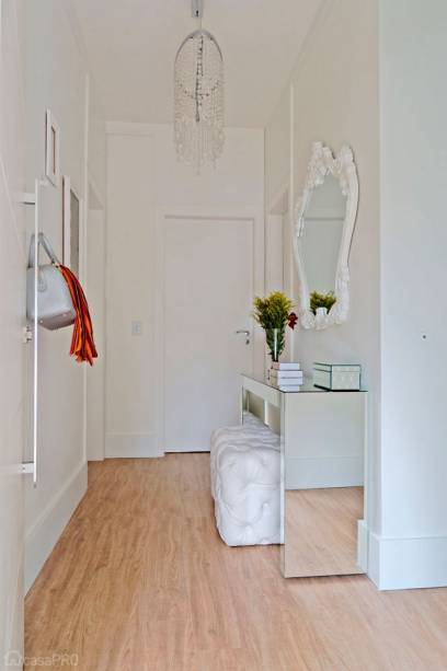 Hall de entrada. O lustre e aparador já eram da moradora e foram reutilizados no hall junto com o espelho novo e os cabides espalhados pela parede de forma harmoniosa. O piso vinílico e as guarnições das portas também são novas benfeitorias que mudaram totalmente o espaço, tornando- o mais claro. Projeto de Elen Saravalli.