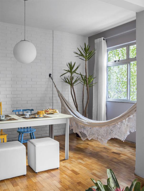 Rede discreta no meio da sala. O clima da sala j&aacute; aponta o que se encontrar&aacute; por todo o apartamento: muitos cantinhos para relaxar. &Eacute; na rede ao lado da mesa que a moradora passa horas apreciando a vista &ndash; a copa de uma &aacute;rvore, luxo para quem mora em um centro urbano.