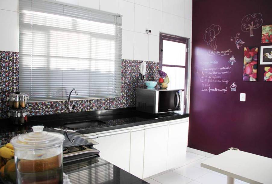 Mãe de dois filhos, Jaqueline de Souza Sobral passa a maior parte de seu tempo na cozinha. Na hora de reformar o ambiente, a única coisa que não abria mão era ter uma parede berinjela. A parede é utilizada como lousa, tanto para Jaqueline fazer anotações, como para sua filha, que gosta de desenhar na parte inferior.