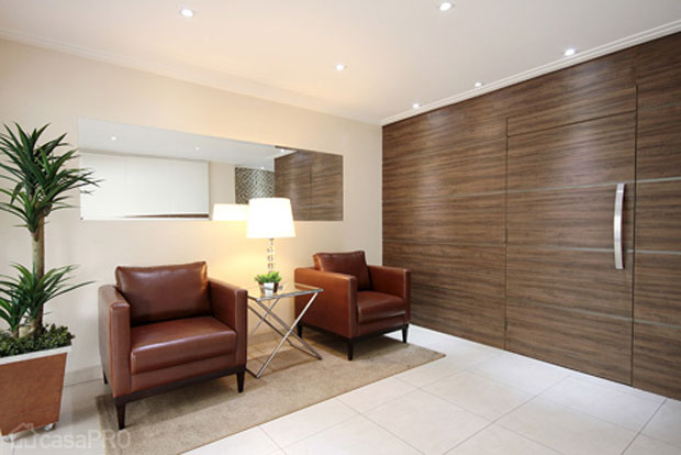 Modernização de hall de entrada. Piso porcelanato, painel com acesso à escada revestido de madeira, o painel do elevador recebeu pastilha de vidro e mármore e o quadro de força é de fórmica branca e detalhe em madeira. Projeto de Ana Paula Santinelo.