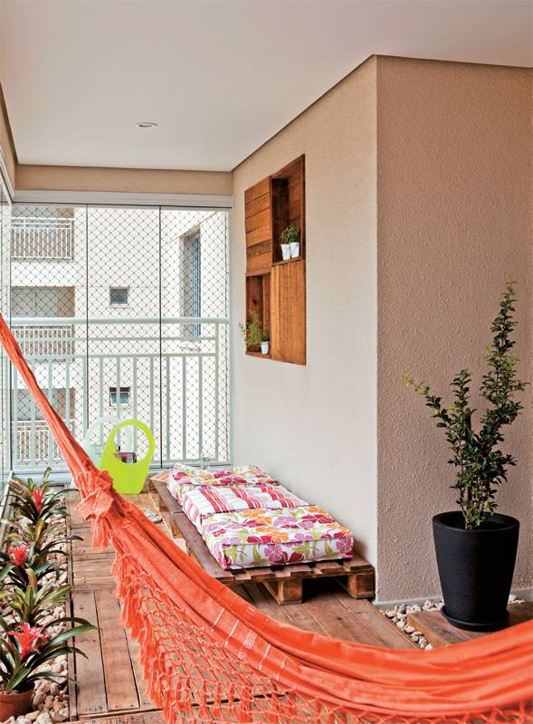 Rede em varanda zen. Neste amplo terra&ccedil;o (6,90 x 2,40 m), foi montado um espa&ccedil;o zen. Para trazer o aconchego da madeira, as designers Cec&iacute;lia Guerra e Cristiane Tamburri, sua s&oacute;cia no escrit&oacute;rio Duo C Design, encomendaram paletes, lixados e envernizados, que fazem as vezes de deque. A rede &eacute; um espa&ccedil;o para descanso em meio &agrave; paisagem da cidade grande e sua cor dialoga com a dos estofados e as flores.