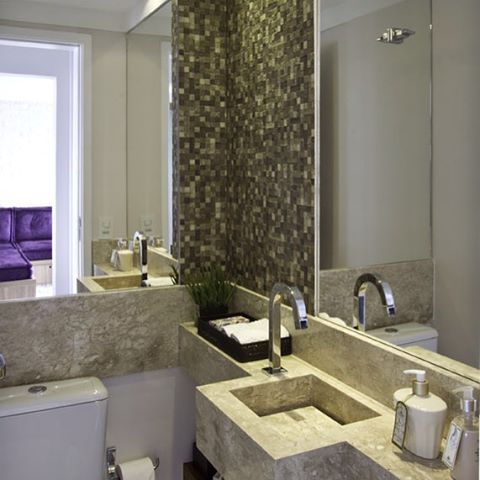 Para criar uma atmosfera rústica, as designers de interiores Christianne Zackiewicz e Vanessa Morgan optaram por porcelanato Amazon Cacao, da Portobello, para uma das paredes, e uma pia com cuba esculpida no mármore travertino. O espaço, de 1,45 m², foi construído em um apartamento na cidade de São Paulo.