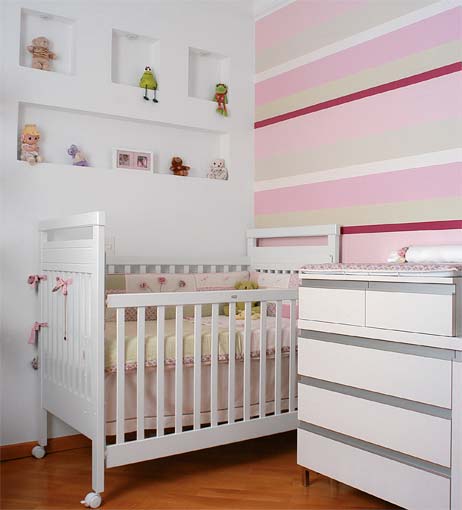 Rosa, verde e branco marcam presença na pintura listrada, no kit de berço e nos móveis. Os nichos no painel de drywall abrigam os primeiros brinquedinhos. O projeto é de Daniela Velloza e Virgínia Velloza.