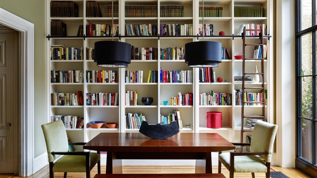 Sala de jantar; mesa de madeira; luminárias pretas; estante branca com livros