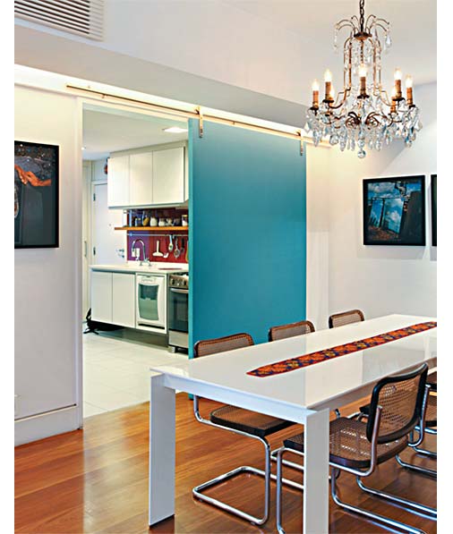 4. Entre a cozinha e a sala de jantar, a porta de correr, um painel único e liso de MDF com 5 cm de espessura, se faz presente como um quadro pintado de azul (Tintas Coral, ref. 36/333) no ambiente. “A intenção era deixá-la marcante, com ferragens aparentes”, diz a arquiteta Renata Bartolomeu. No teto, um rasgo em forma de L acompanha a viga invertida e embute iluminação indireta.