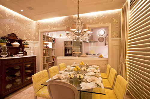 CASACOR Bahia - Toda revestida de papel de parede com motivo floral, a Cozinha da CASACOR Bahia, assinada pelas arquitetas Claudia e Daniela Lopes, abriga também um espaço de copa. As arquitetas se inspiraram na cor dos limões sicilianos para criar este ambiente. A cozinha tecnológica contrasta com o ambiente feminino da copa. Um dos destaques do ambiente é a cristaleira antiga reformada. As cadeiras do lado esquerdo da mesa são revestidas de tecidos com estampas. As do lado direito têm estofado liso na cor do limão siciliano.