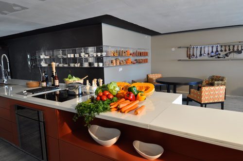 CASACOR Pernambuco - O Lounge Gourmet, assinado pelo arquiteto Carlos Augusto Lira, possui uma ilha com balcão de marmoglass. O visitante pode apreciar o ambiente sentado em poltronas com diferentes estampas. Na parede, ao fundo, colheres de madeiras e peças de barro, da coleção do próprio arquiteto, remetem ao artesanato popular.