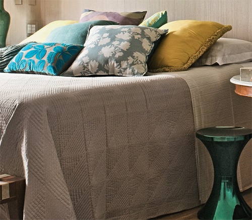 Almofadas de diferentes nuances alegram a cama, coberta com colcha de algod&atilde;...