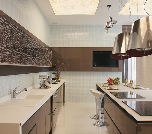 CASACOR Rio de Janeiro - Uma ilha central, com bancada de vidro acidado, dois cooktops e espaço para refeições rápidas, é o foco de atenções na cozinha projetada pelos arquitetos Ana Lila Denton e A. Juarez Farias Jr. Queríamos montar um espaço prático, mas sem deixar de ser elegante, afirma Ana Lila. Nos armários, portas de vidro serigrafado conferem um ar futurista no ambiente ao lado das duas coifas-luminárias de alumínio. Nas paredes, pastilhas de vidro foscas e brilhantes se misturam aleatoriamente e, no teto, rasgos de luz foram cobertos com tensoflex estampado.